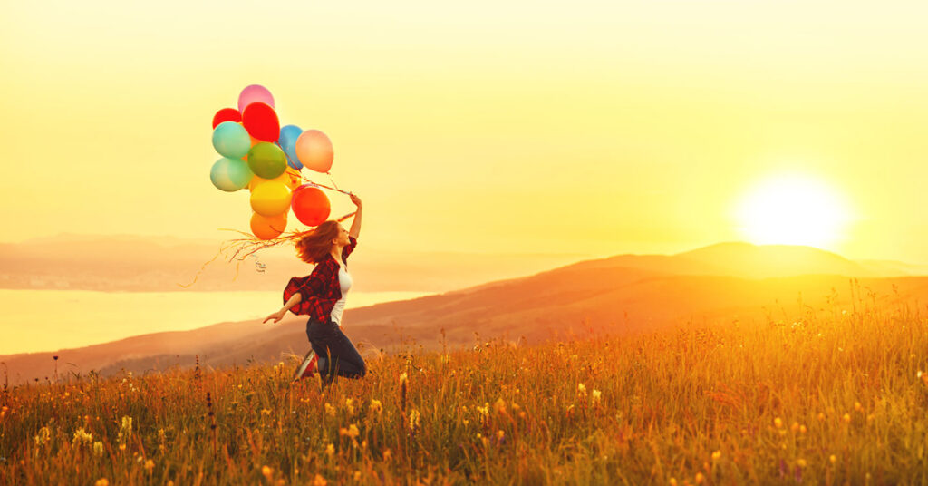 running with balloons in a field with sunshine to demonstrate authentic happiness